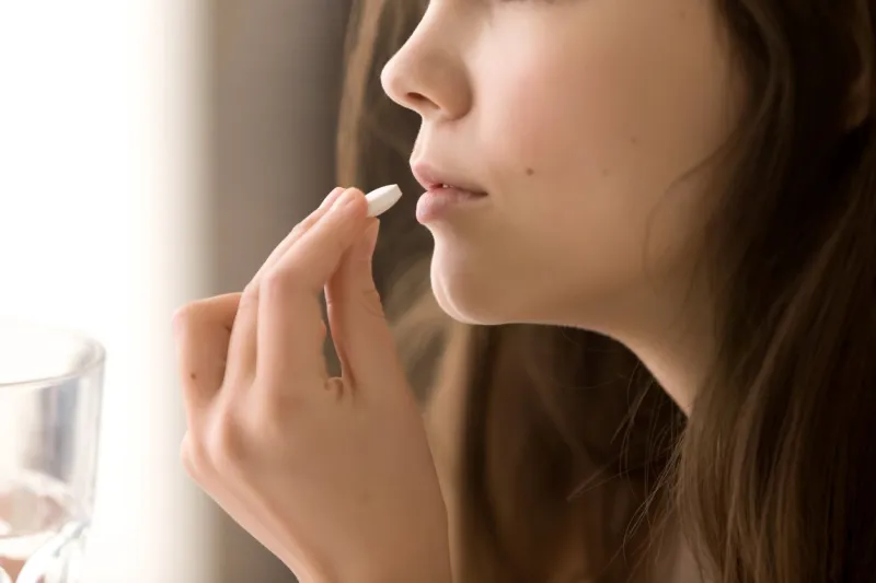 close up image of woman putting white round pill in mouth sick female taking medicines, antidepressant, painkiller or antibiotic young lady drinking contraceptives pharmacy and healthcare concept