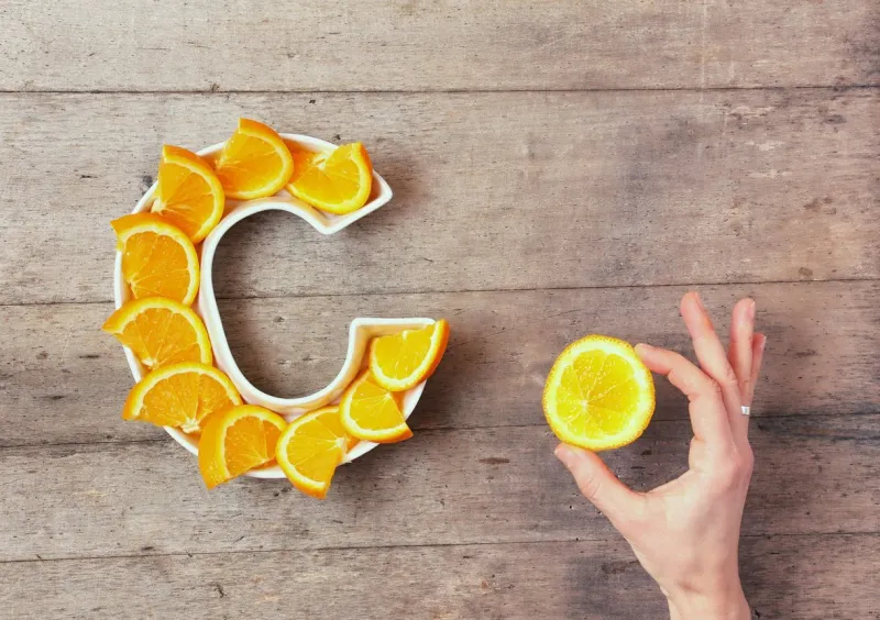 vitamin c or ascorbic acid nutrient in food concept plate in shape of letter c with orange slices and woman's hand with citrus making sign ok on wooden background flat lay or top view