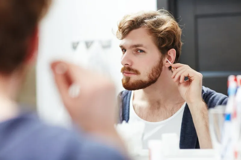 young man cleaning his ears in front of mirror