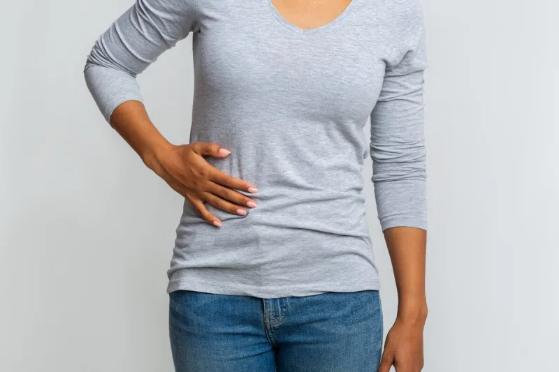 cropped of black girl holding her side, suffering from acute liver pain, grey background