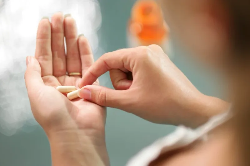 close up view of young woman holding ginseng vitamins and minerals pills in hand with capsule bottle on table high angle view