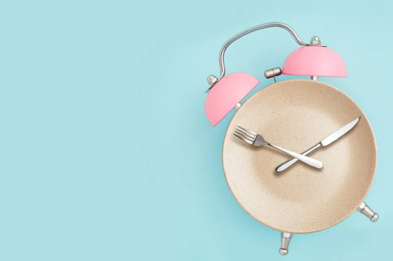 alarm clock and plate with cutlery concept of intermittent fasting, lunchtime, diet and weight loss