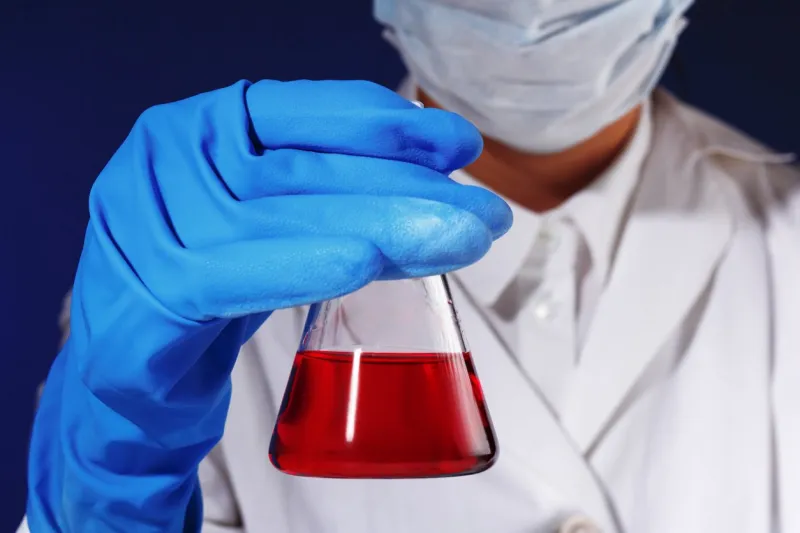 in a chemistry lab, a female chemist is analyzing a flask with red liquid medical experiment