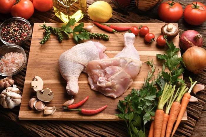 fresh raw chicken thighs with ingredients for cooking on a wooden cutting board