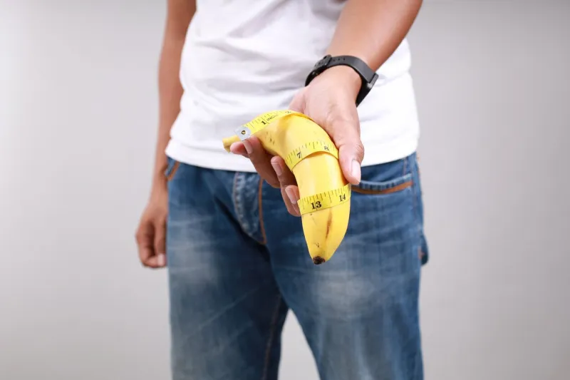 asian man holding a banana with tape measure size matters concept and penis size measurement