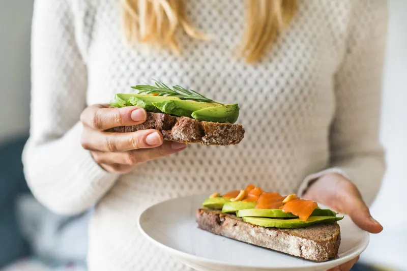 close up of woman holding plate with avocado toast as fresh snack, day light