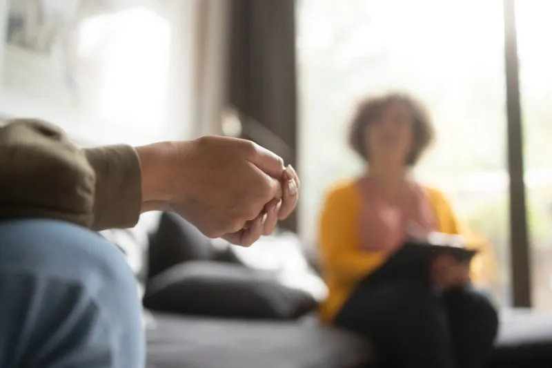 close-up photo of a teenage girl's hands with fingers crossed nervously she is in a therapy session with her psychotherapist