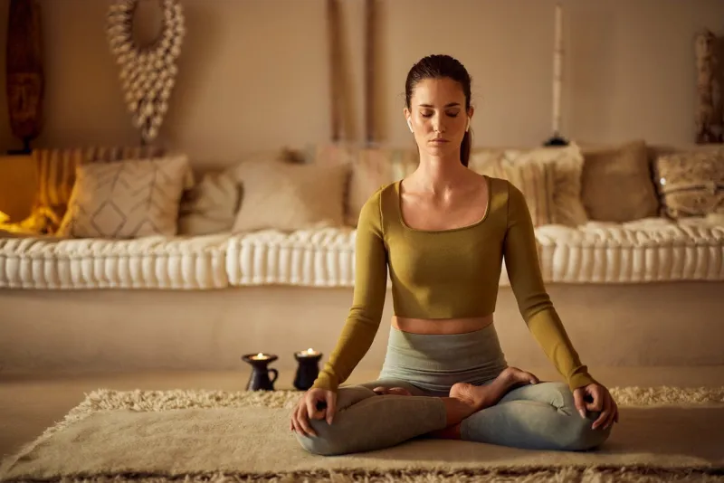 a portrait of a woman doing meditation at home, keeping her eyes closed, has candles on the side