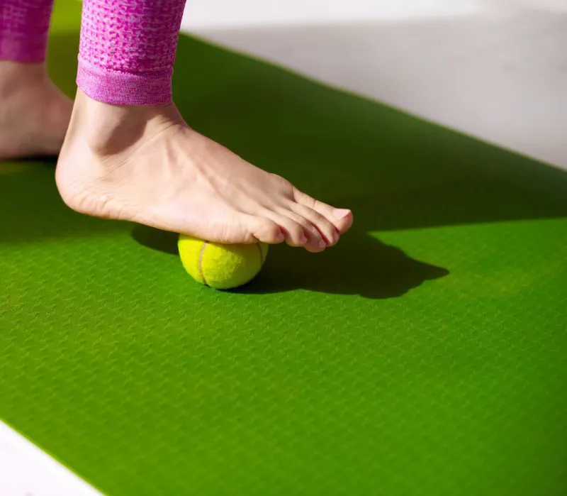 a tennis ball under female foot massage for relieve muscle tension, improve circulation, and plantar fasciitis relief physiotherapy, reflexology, and flexibility promotion concept