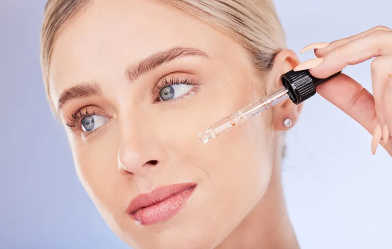 face, beauty and skincare of woman with serum in studio isolated on a blue background dermatology cosmetics, thinking closeup and female model apply hyaluronic acid, retinol or essential oil product