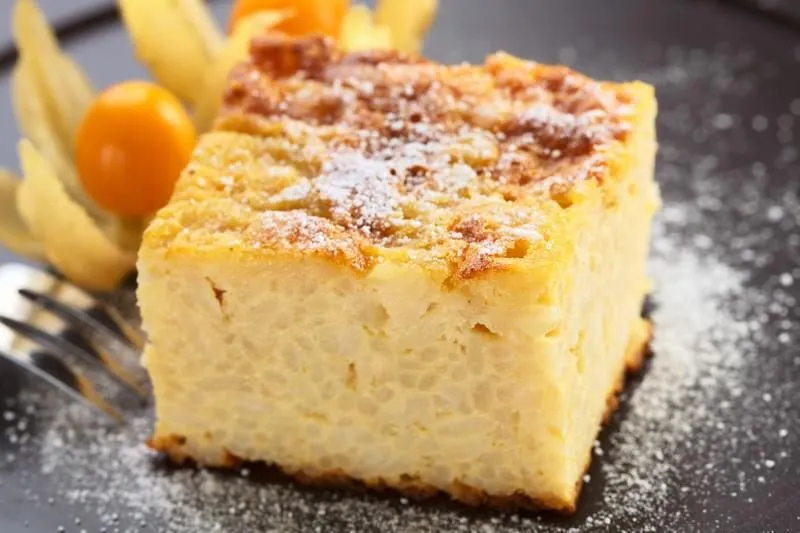 riz au lait cuit dessert sucré avec de la poudre de sucre et garni de physalis dans le dos avec une fourchette sur le côté (très faible profondeur de champ, se concentrer sur le coin avant droit du gâteau)