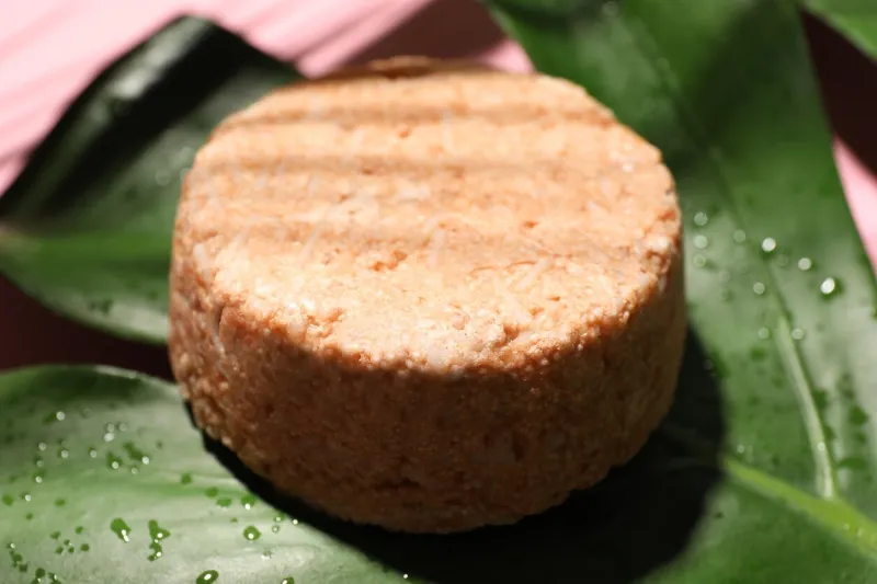 solid shampoo bar and leaf on pink background, closeup hair care