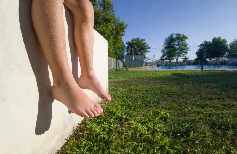 barefoot boy sitting in the sun in a public swimming pool bone development in children concept