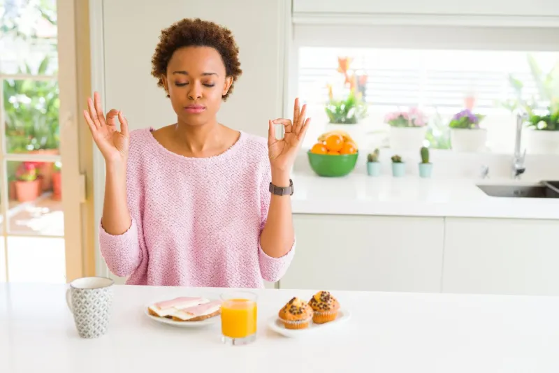young african american woman eating breaksfast in the morning at home relax and smiling with eyes closed doing meditation gesture with fingers yoga concept
