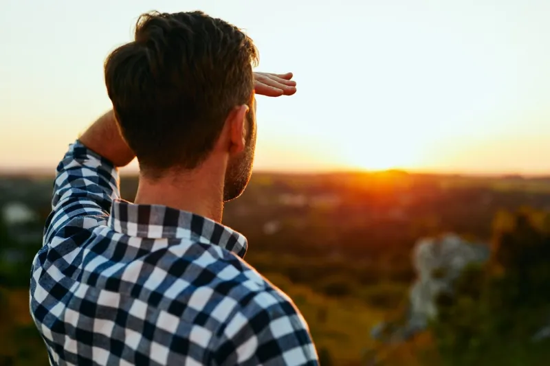 man standing on meadow in mountains and admiring sunset