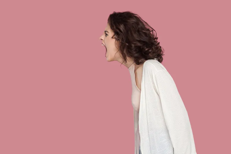 profile side view portrait of brunette young woman with curly hairstyle in casual style standing and screaming people expression and emotion indoor studio shot isolated on pink background