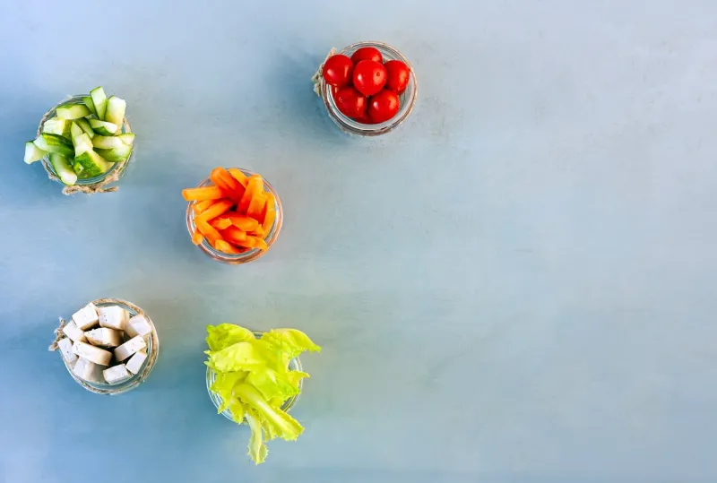 top view of carrots, tofu, lettuce, cherry, cucumbers cut into thin strips, served in a glass cups as a snack healthy breakfast concept space for text