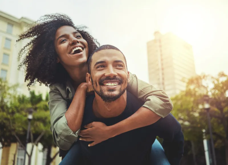 cheerful young man giving piggyback ride to his girlfriend outdoors in the city