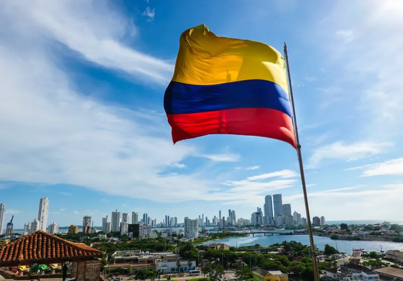 the colombian flag waving in the wind blue sky with white clouds in the background the city of cartagena is in the far back shot in cartagena, colombia, usa