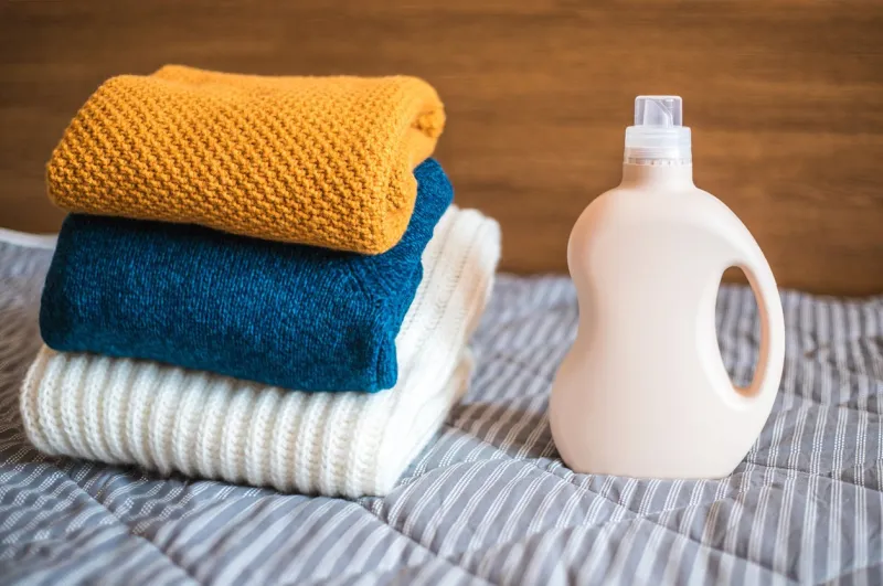 bottle of detergent and a pile of clean colored sweaters on the bed at home
