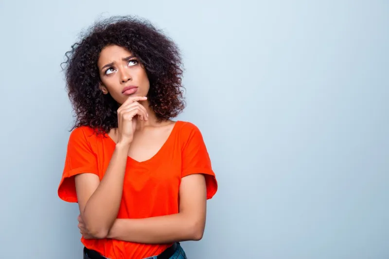 portrait with copy space empty place of thoughtful minded woman with modern hairdo holding hand on chin looking up trying to find solution isolated on grey background