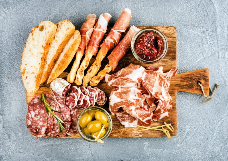 meat appetizer selection or wine snack set variety of smoked meat, salami, prosciutto, bread sticks, baguette, olives and sun-dried tomatoes on rustic wooden board, top view, horizontal