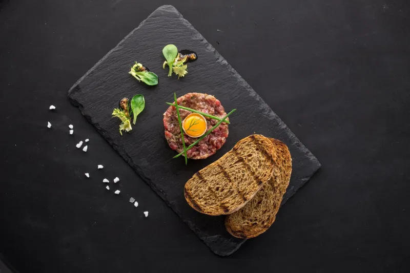 steak tartare with bread toasts served on a stone plate top view on black background studio shot