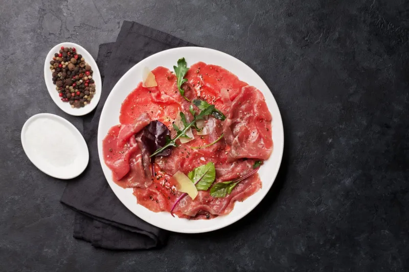 marbled beef carpaccio with arugula, lemon and parmesan cheese top view, flat lay with copy space
