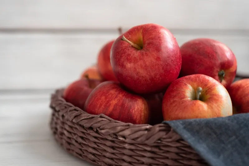 fresh red apples in a wicker basket ripe fruits as a concept of a plentiful harvest white background wooden table