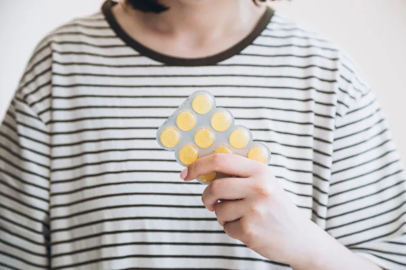 woman holding blister with yellow cough drops, blister package of lemon pills medical lozenges for relief cough, sore throat and throat irritation cough and colds drop colorful cough pastille