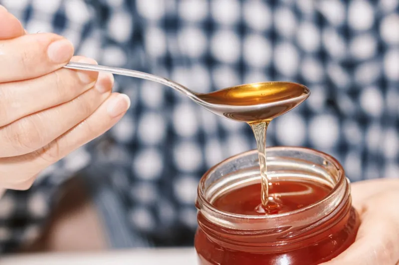 woman hand holding glass jar of honey