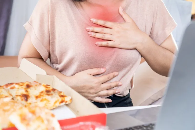 woman suffering from chest pain , heartburn caused by acid reflux after eating junk food pizza