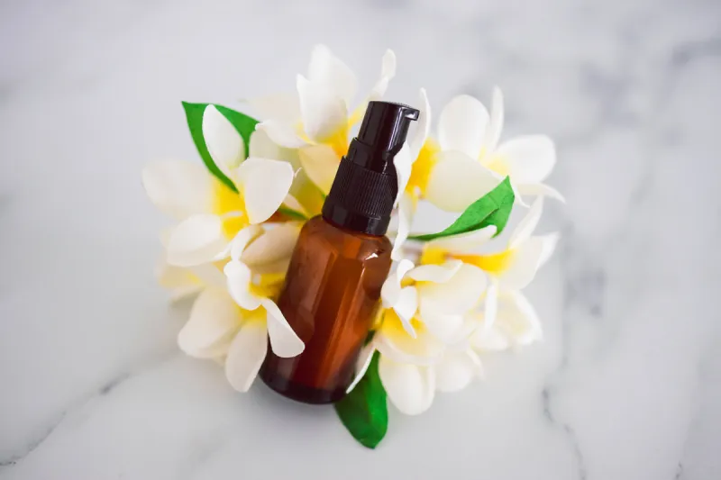 natural beauty and organic ingredients in skincare, apothecary skincare bottle with tropical frangipani flowers in the background