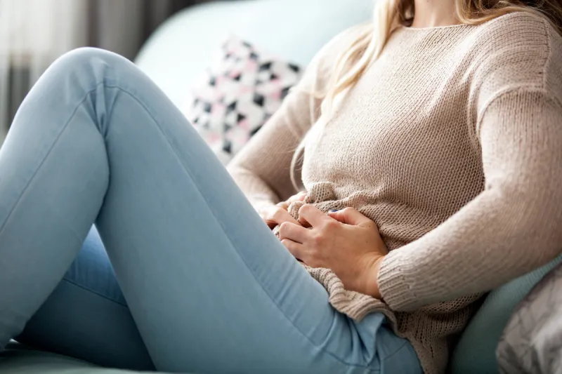 young woman suffering from abdominal pain while sitting on sofa at home