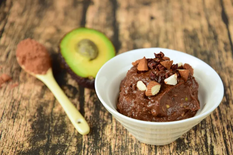 delicious vegan chocolate mousse with banana, avocado, cocoa powder and maple syrup garnish with almond nuts and cacao nibs