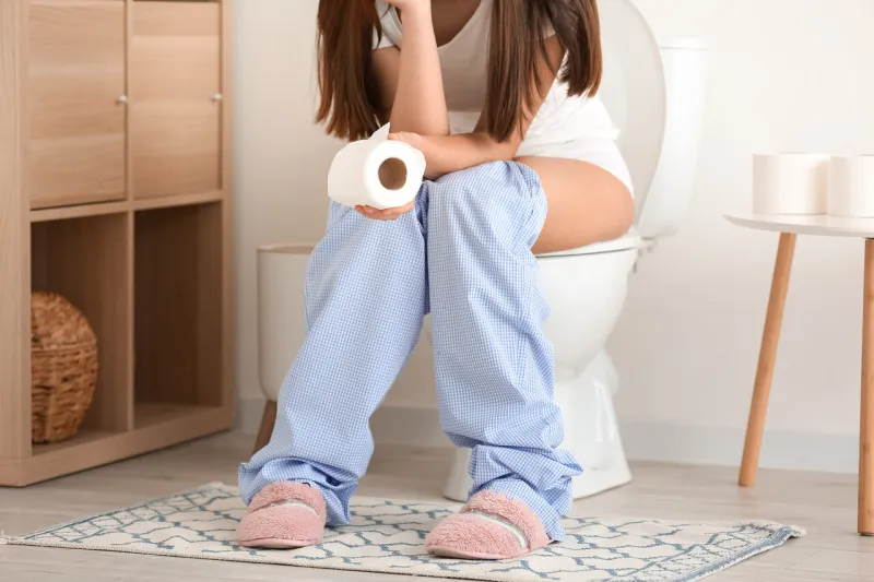young woman with paper roll sitting on toilet bowl in restroom