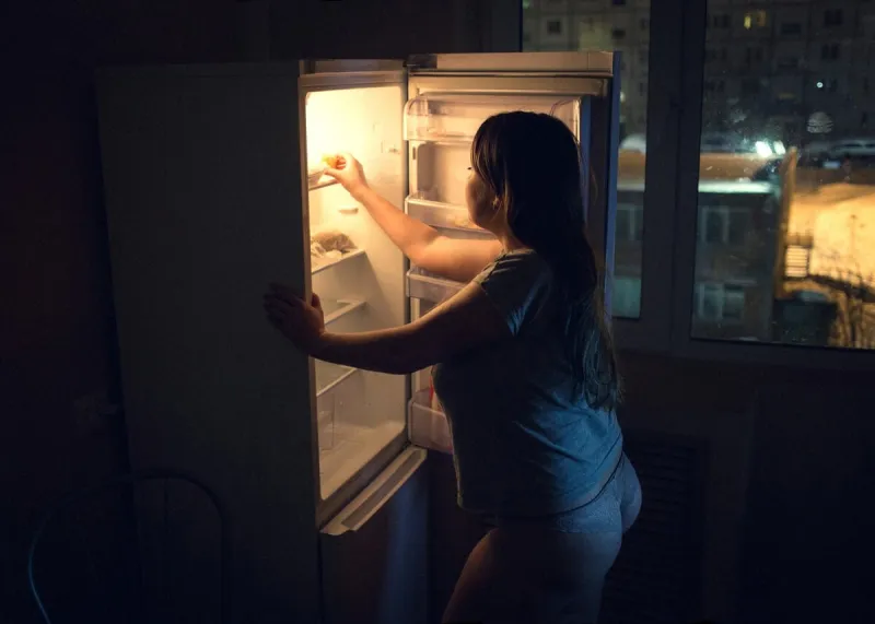 sexy chubby woman craving and looking for food in a frige late at night girl dressed in homewear t-shirt and panties authentic atmosphere of the kitchen grainy high iso image