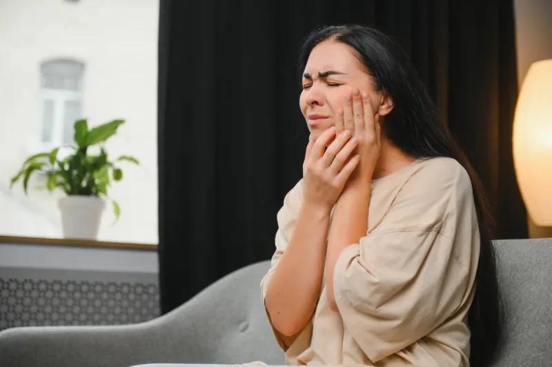 woman with severe toothache touching her swollen cheek young girl feeling discomfort after tooth extraction upset lady with inflamed tooth nerve or terrible dental pain sitting on sofa at home