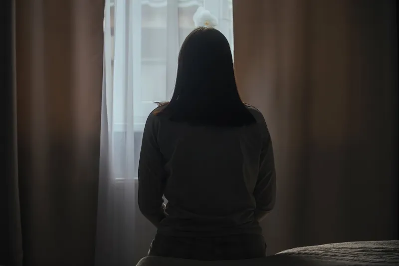 silhouette of a young woman in pajamas against the background of a window at home on a bed with seasonal affective disorder or depression the concept of winter depression due to lack of sunlight
