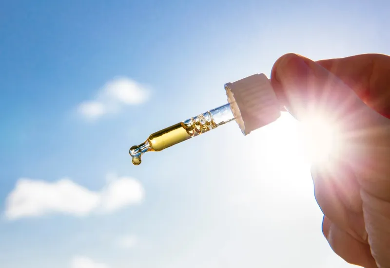 hand holding dropper pipette with nice golden liquid d-vitamin against sun and blue sky on sunny day vitamin d keeps you healthy while lack of sun in winter, cure concept