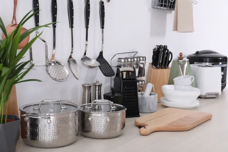 set of clean cookware, dishes, utensils and appliances on table at white wall