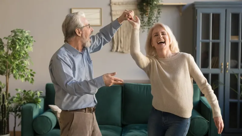 joyful active old retired romantic couple dancing laughing in living room, happy middle aged wife and elder husband having fun at home, smiling senior family grandparents relaxing bonding together