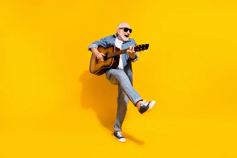 full length photo of cool happy positive old man dance hold guitar wear sunglass isolated on yellow color background