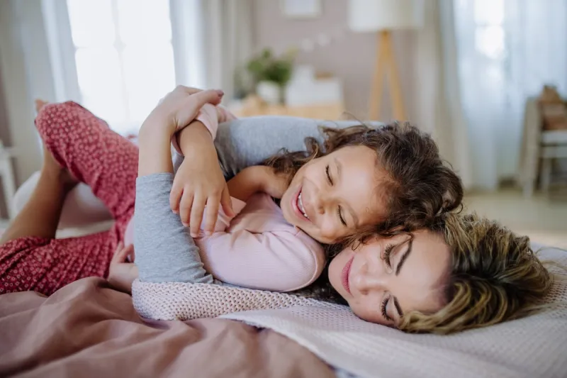 a happy mother lying on bed with her little daughter and cocoonning at home