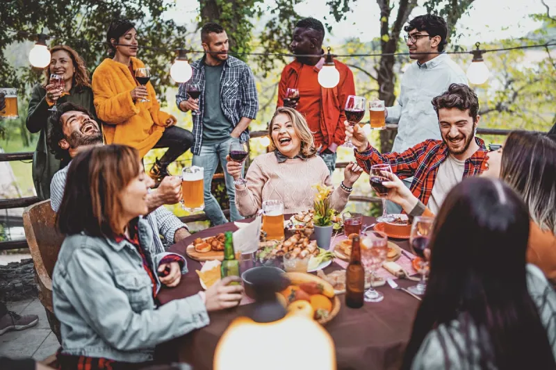 young friends having fun drinking beer and wine on balcony at farmhouse dinner pic nic party - hipster millennial people eating bbq food at fancy restaurant together - dinning life style concept