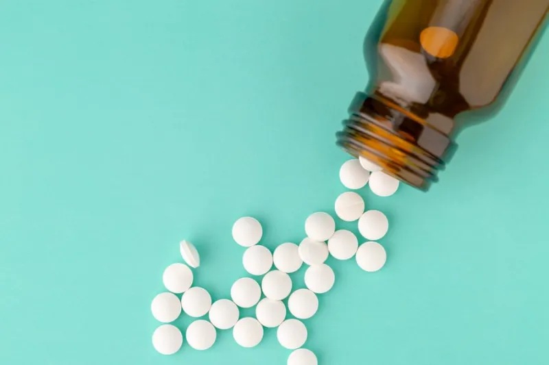 white round tablets scattered in front of glass bottle of pills