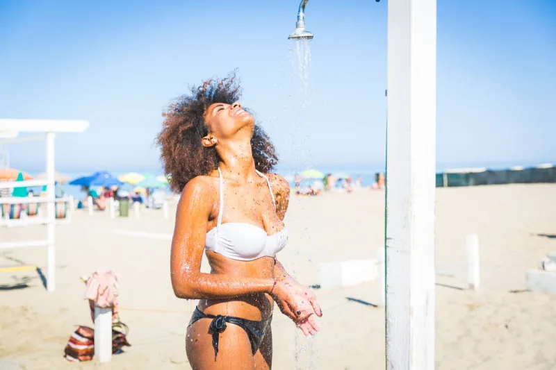 young black woman having a shower in the beach after swimming and sunbathing she is twenty years old, mixed race caucasian and african black, with curly and voluminous hair