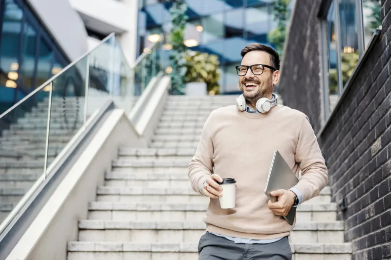 a casual businessman rushing to the office with coffee and laptop in hands