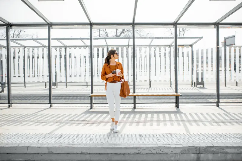 woman standing alone at the public transport stop on a sunny day outdoors concept of a transportation and urban life