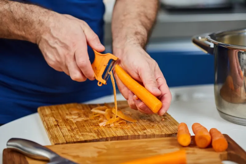 man peeling carrots on a wooden board